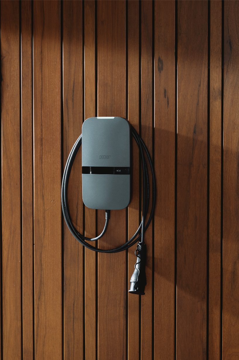 Peblar-laadpaal met opgerolde laadkabel aan een houten wand